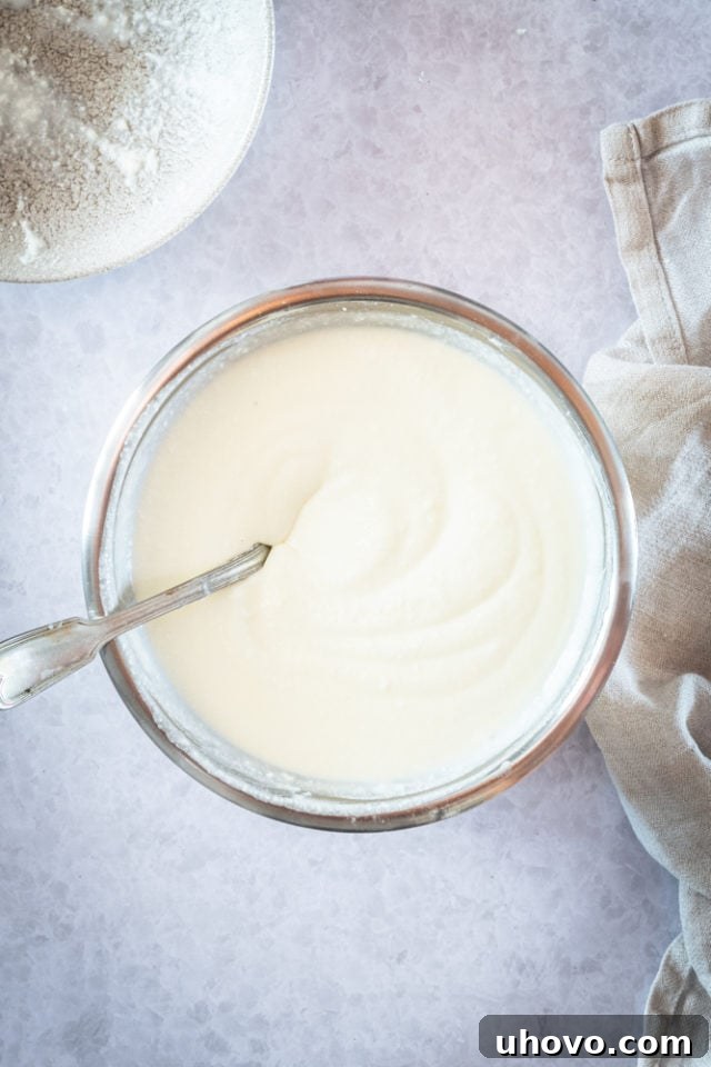 Overhead view of heavy cream being whipped in a glass mixing bowl, forming soft peaks.