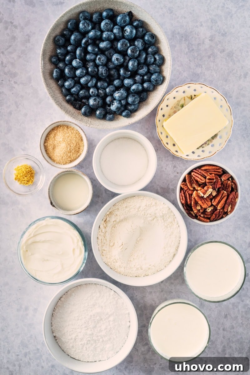 Overhead view of fresh blueberries, sugar, cornstarch, butter, flour, pecans, heavy cream, cream cheese, and confectioners' sugar laid out as ingredients for Blueberry Jamboree.