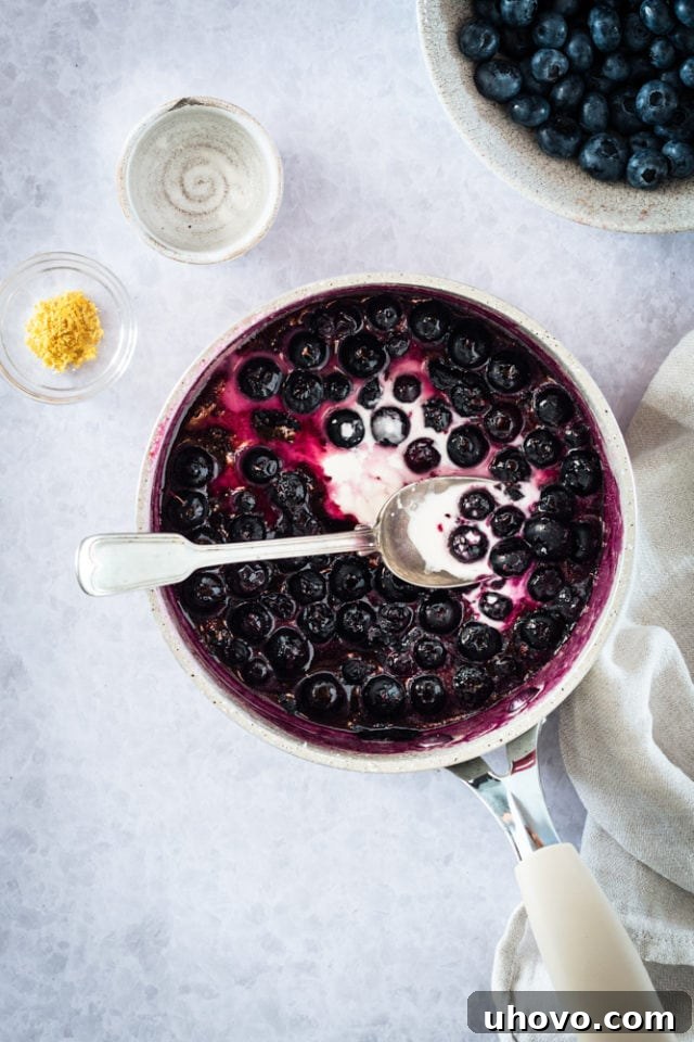 Overhead view of the blueberry mixture simmering in a pan, thickening into a saucy consistency after adding the cornstarch slurry.