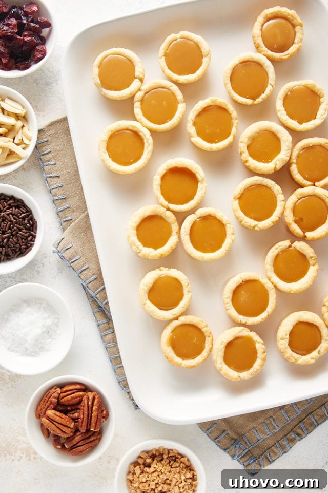 overhead view of Mini Caramel Tarts on a white serving tray with various toppings alongside