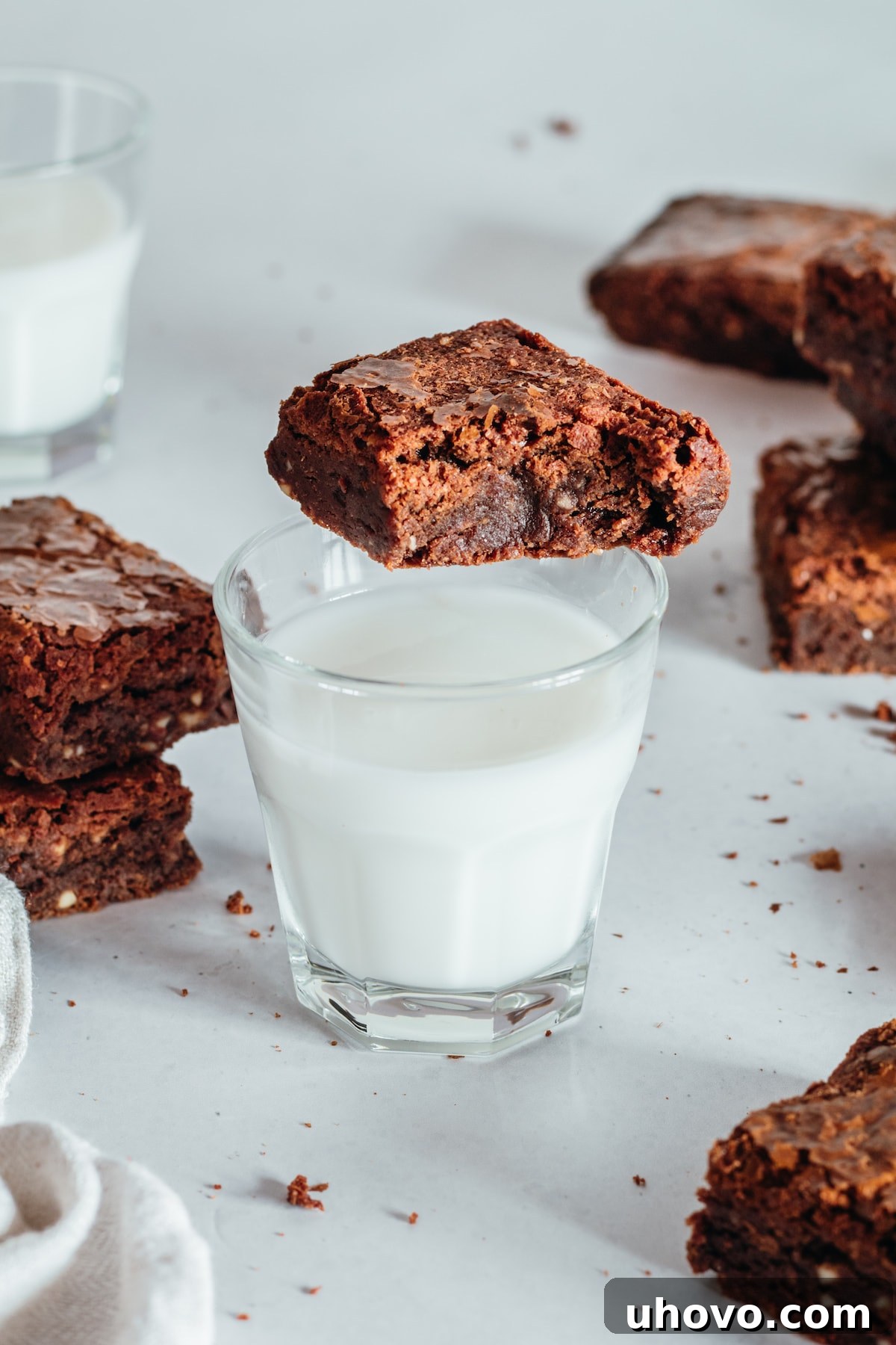 A refreshing cup of milk with a Supernatural Brownie resting on its edge, and additional brownies in the background, creating a classic dessert scene