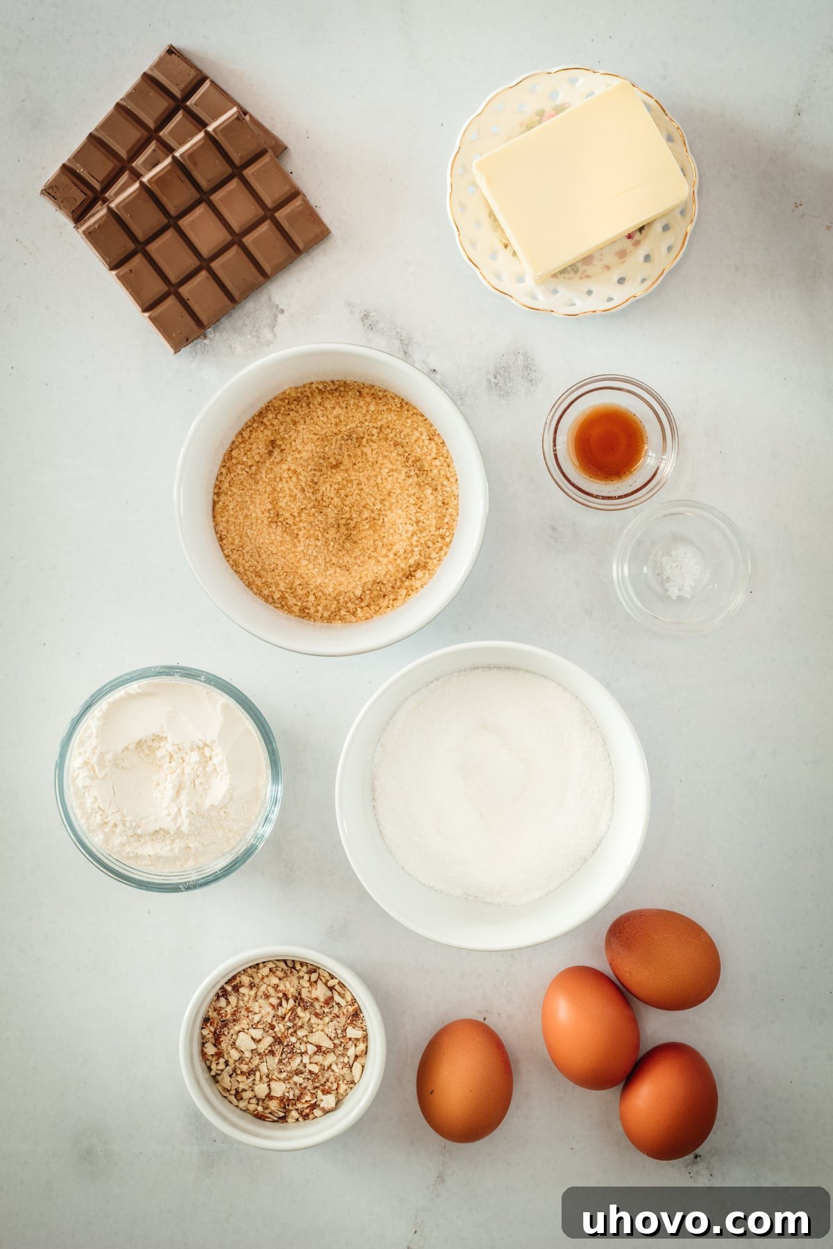 Overhead view of all the Supernatural Brownie ingredients laid out: butter, chocolate, eggs, salt, sugars, vanilla, flour, and chopped nuts