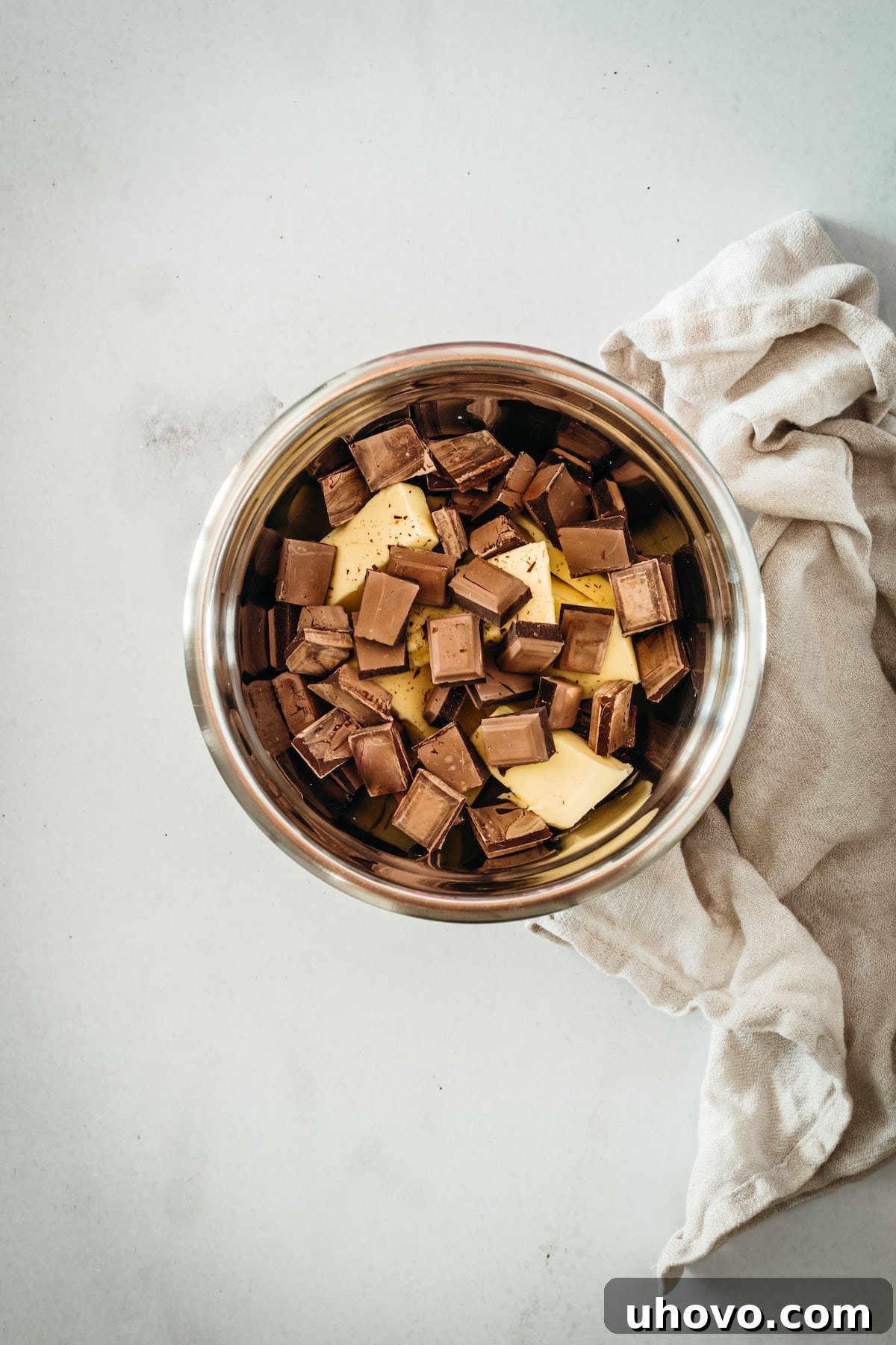 Overhead view of bittersweet chocolate pieces and cubes of unsalted butter in a metal bowl, ready for melting