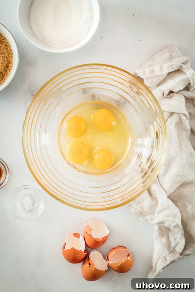 Overhead view of 4 large room-temperature eggs cracked into a clear glass mixing bowl