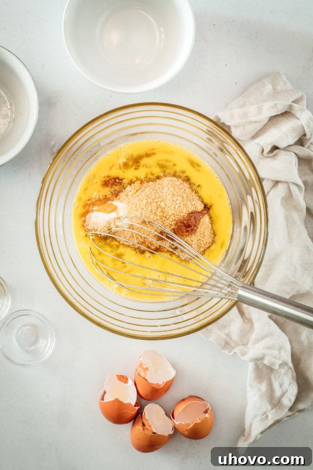 Overhead view of eggs and both granulated and dark brown sugar in a mixing bowl with a whisk, ready to be combined