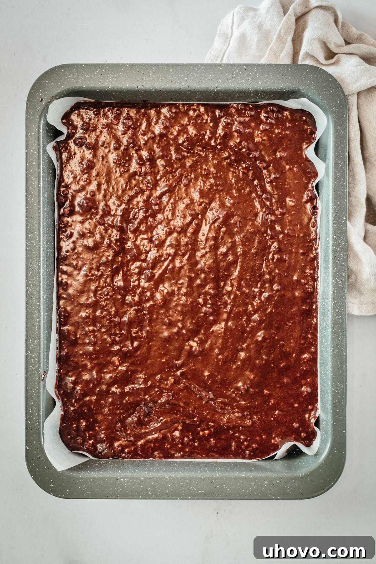 Overhead view of rich brownie batter spread evenly in a parchment-lined baking pan, ready for the oven