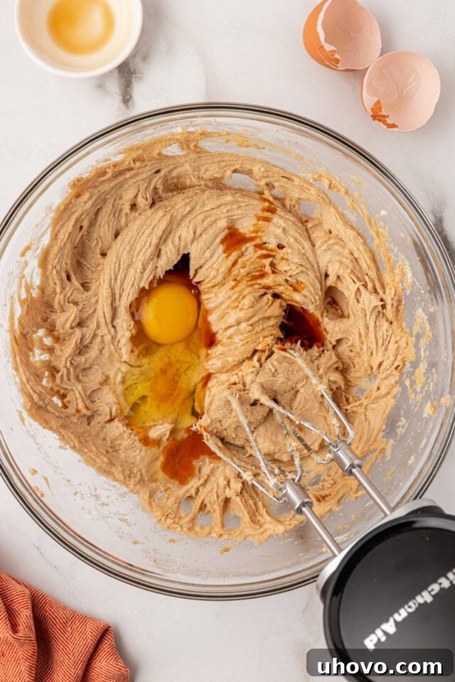 overhead view of egg and vanilla extract added to creamed butter, cream cheese, and brown sugar