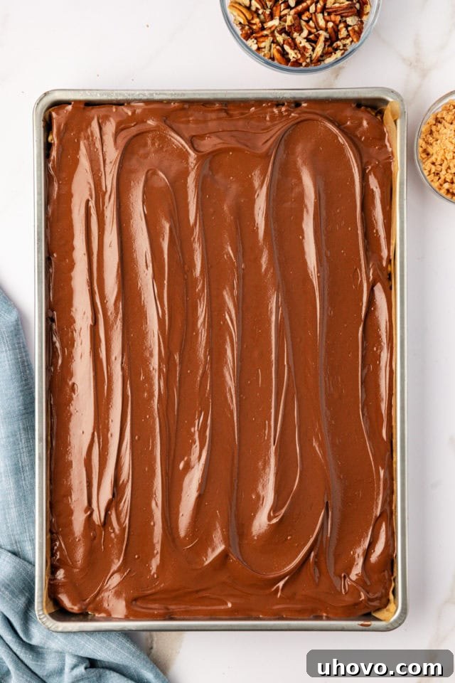 The smooth chocolate-peanut butter topping being spread over the cereal layer of the bars, creating a rich, glossy finish.