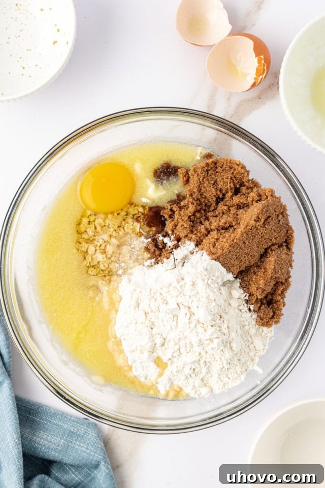 Overhead view of a glass mixing bowl filled with the dry crust ingredients—quick oats, dark brown sugar, and all-purpose flour.