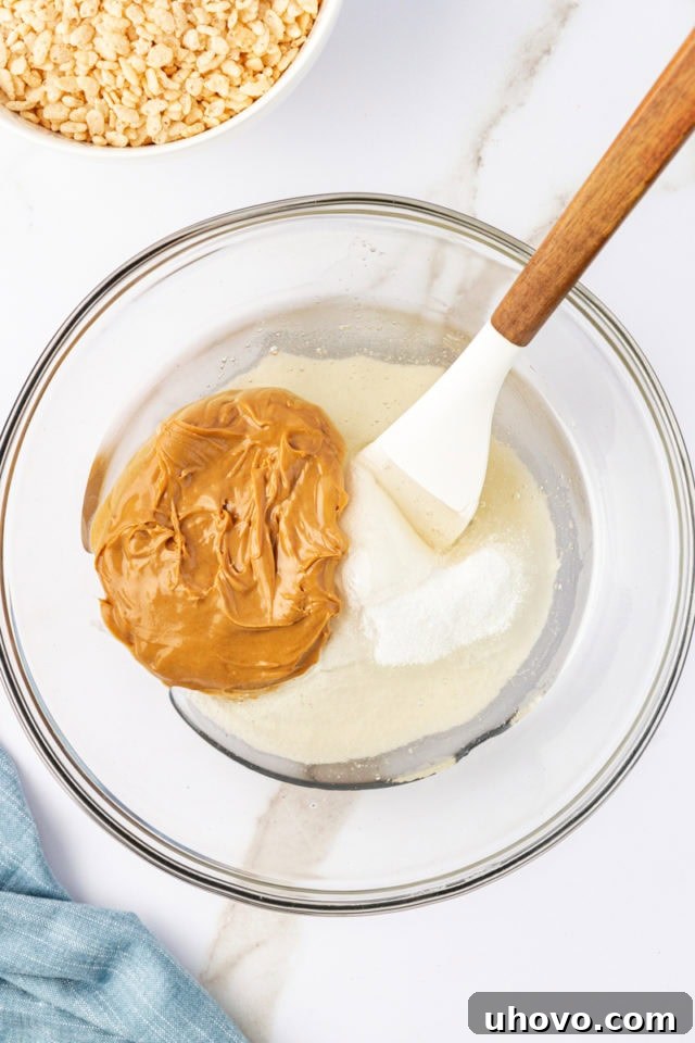 Overhead view of a glass mixing bowl containing creamy peanut butter, granulated sugar, and light corn syrup, ready to be melted.