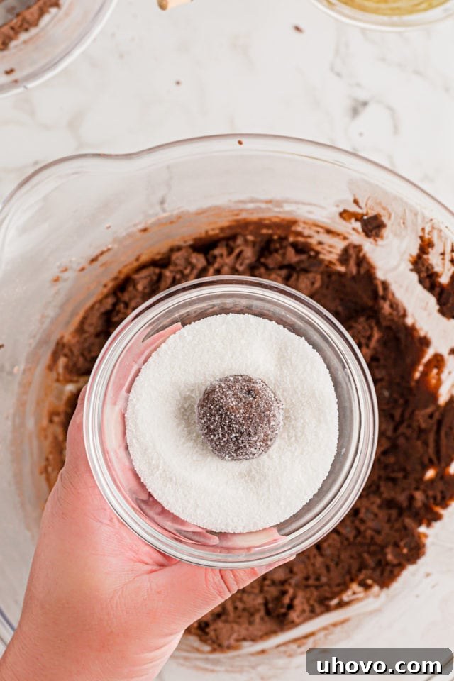 A ball of Double Chocolate Brownie Cookie dough being rolled in a bowl of granulated sugar