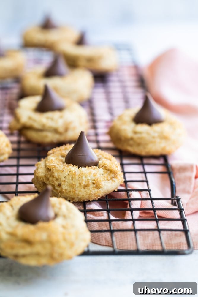 A stack of golden brown Chocolate Caramel Kiss Cookies, some with melted chocolate and others with perfect kisses, on a wire cooling rack.