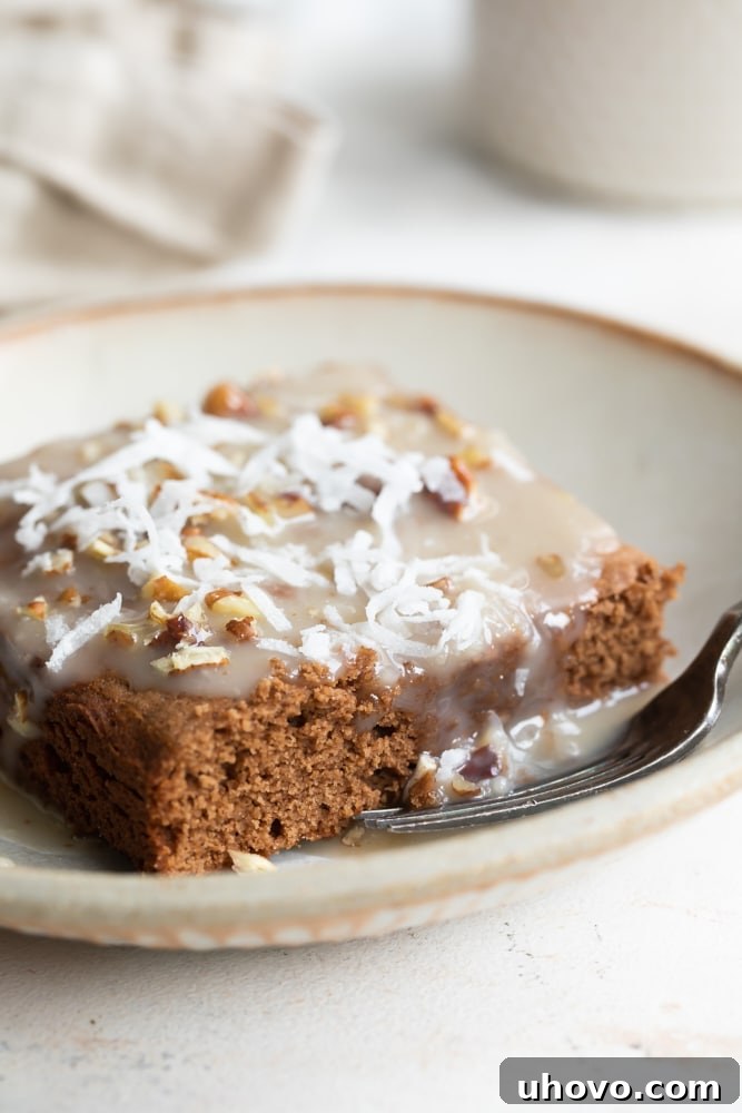 A stunning close-up of a square of German chocolate cake, featuring the rich chocolate base and a generous topping of the warm coconut-pecan sauce, resting on a beige plate with a fork poised for a bite.