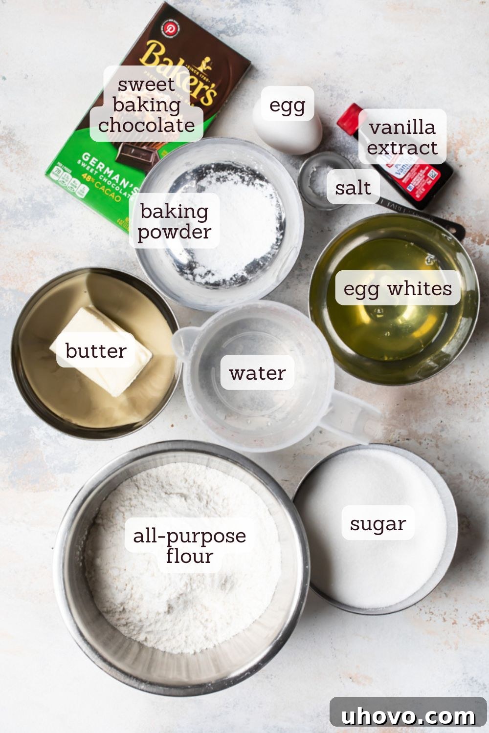 An overhead view of carefully arranged ingredients for German chocolate cake, including flour, sugar, chocolate chunks, butter, and eggs, ready for baking.