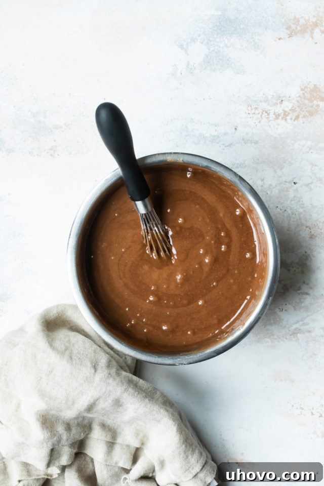 Creamy, smooth cake batter being whisked in a large metal mixing bowl, showing a consistent texture.