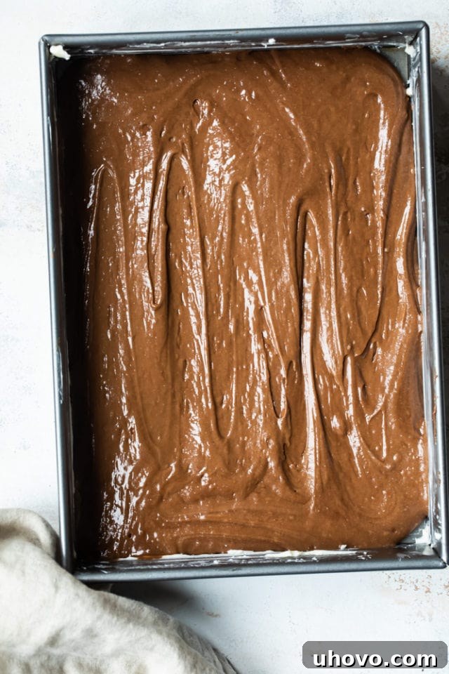 Smooth, glossy German chocolate cake batter spread evenly within a 9x13 inch baking pan, ready for the oven.