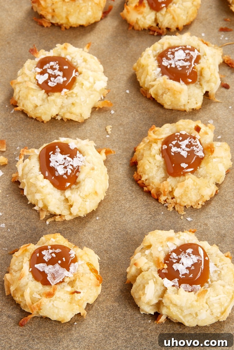 Overhead view of several Coconut-Salted Caramel Thumbprint Cookies arranged on parchment paper, highlighting their perfect shape and glistening caramel.