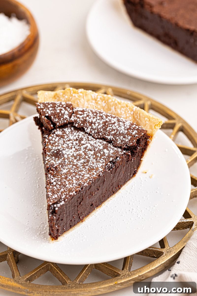 a close-up slice of hot fudge pie, simply topped with a delicate dusting of confectioners' sugar, on a white plate