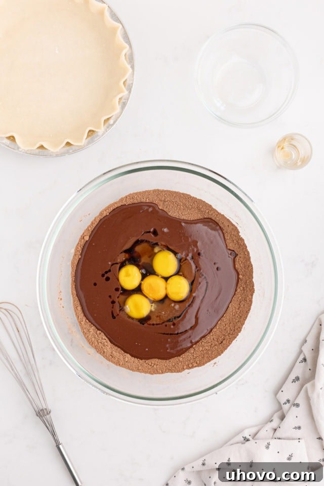 overhead view of whole eggs and egg yolks being added to the melted chocolate mixture for hot fudge pie
