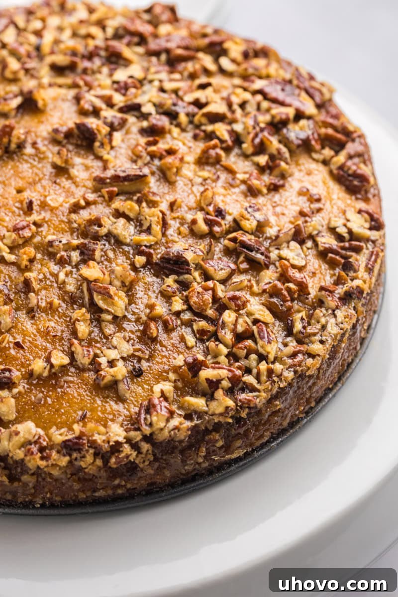 A stunning, whole Pecan Pie Coffee Cake artfully displayed on an elegant white cake stand, showcasing its golden crust and invitingly gooey pecan topping.