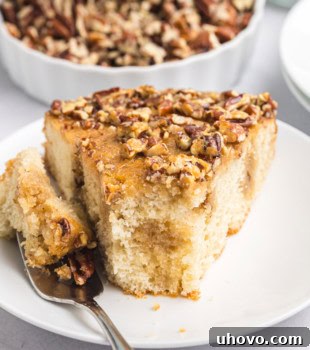 A slice of Pecan Pie Coffee Cake on a white plate with a bite on a fork, highlighting its tender texture and rich topping.