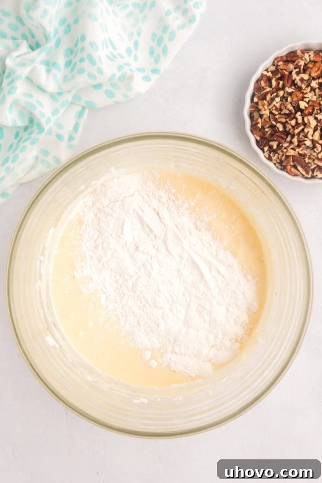 Close-up, overhead view of the coffee cake batter in a glass bowl, with dry flour mixture gently folded into the wet ingredients, illustrating the alternating addition process.