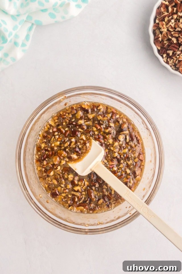 An overhead close-up of a rich, gooey pecan pie coffee cake topping mixture, complete with chopped pecans, swirling in a glass mixing bowl, ready to be poured.