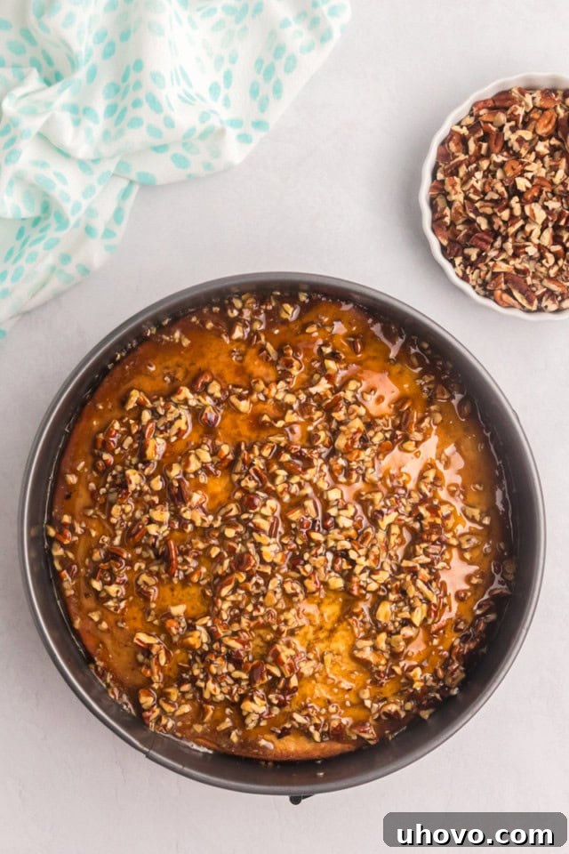 Close-up, overhead view of the Pecan Pie Coffee Cake with the glossy, rich pecan topping being generously poured over the cake's surface, slowly seeping into the poked holes.