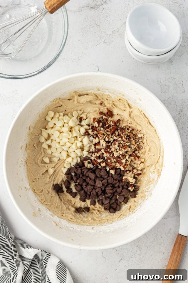 Overhead view of chocolate chips and pecans added to bowl of cookie dough
