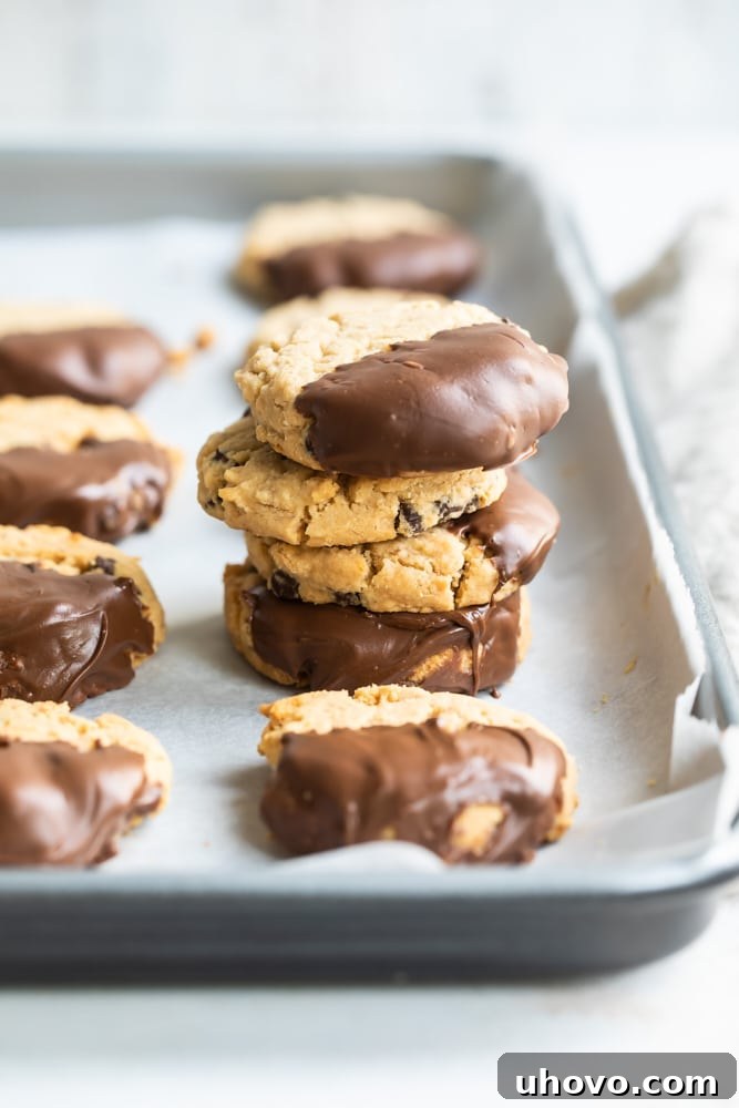 Chocolate-Dipped Peanut Butter Meltaway Cookies stacked on a parchment-lined baking sheet