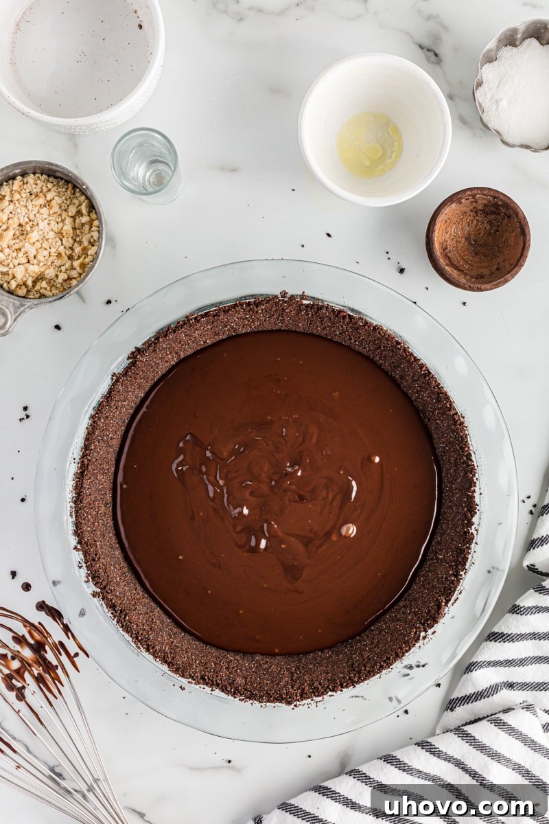 Overhead view of the glossy chocolate ganache being poured into the baked chocolate pie crust.