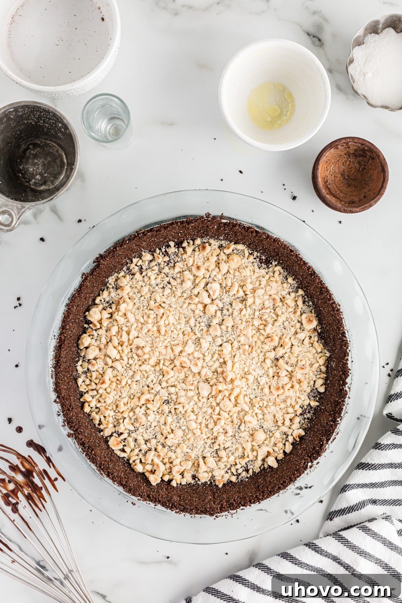 Overhead view of coarsely chopped toasted hazelnuts being sprinkled over the top of the smooth chocolate ganache in the pie crust.