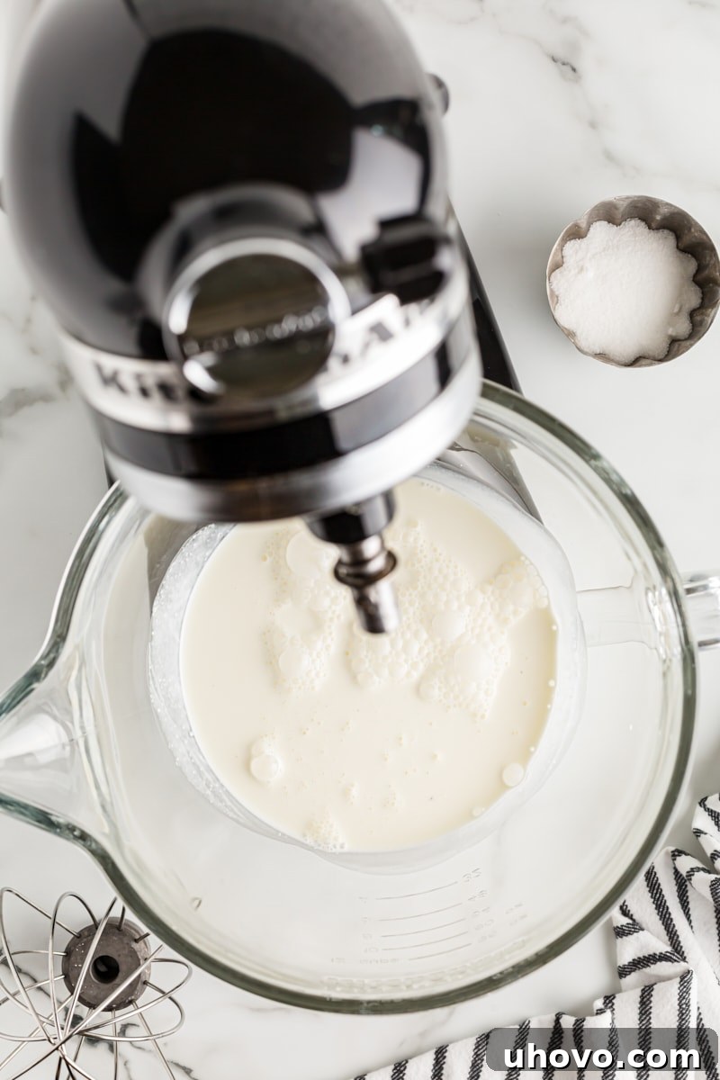 Overhead view of cold heavy cream in a stand mixer bowl, ready to be whipped.