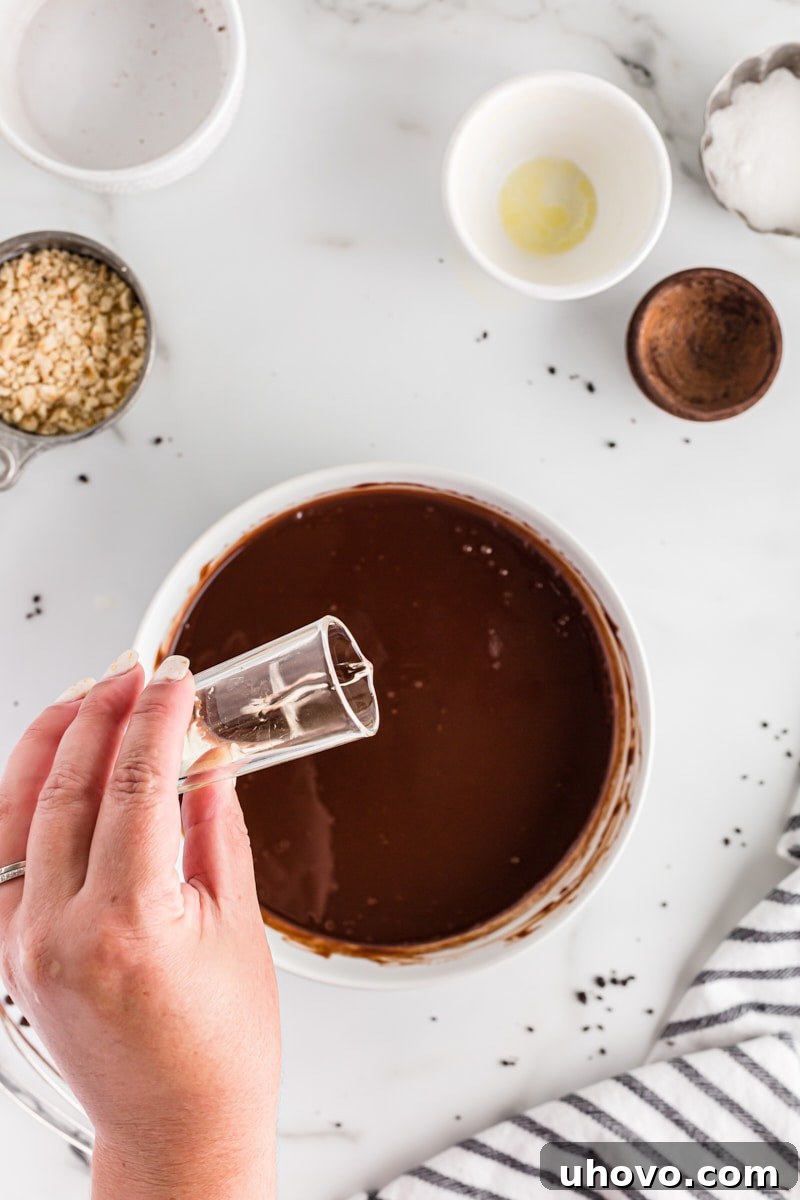 A hand pouring Frangelico hazelnut liqueur into a bowl of rich, melted chocolate ganache, adding a crucial layer of flavor.