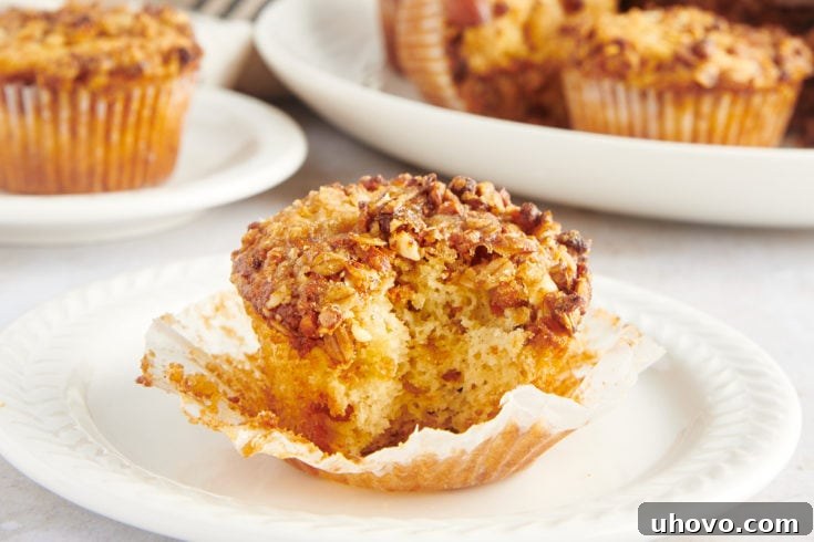 Granola yogurt muffin on white plate with wrapper removed, bite taken out to show texture