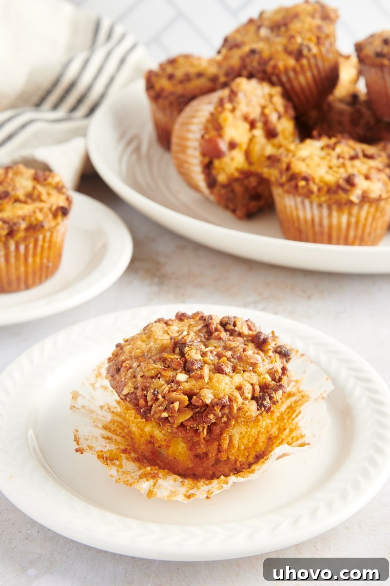 A single granola yogurt muffin, unwrapped and displayed on a white plate, revealing its tender interior and crispy topping.