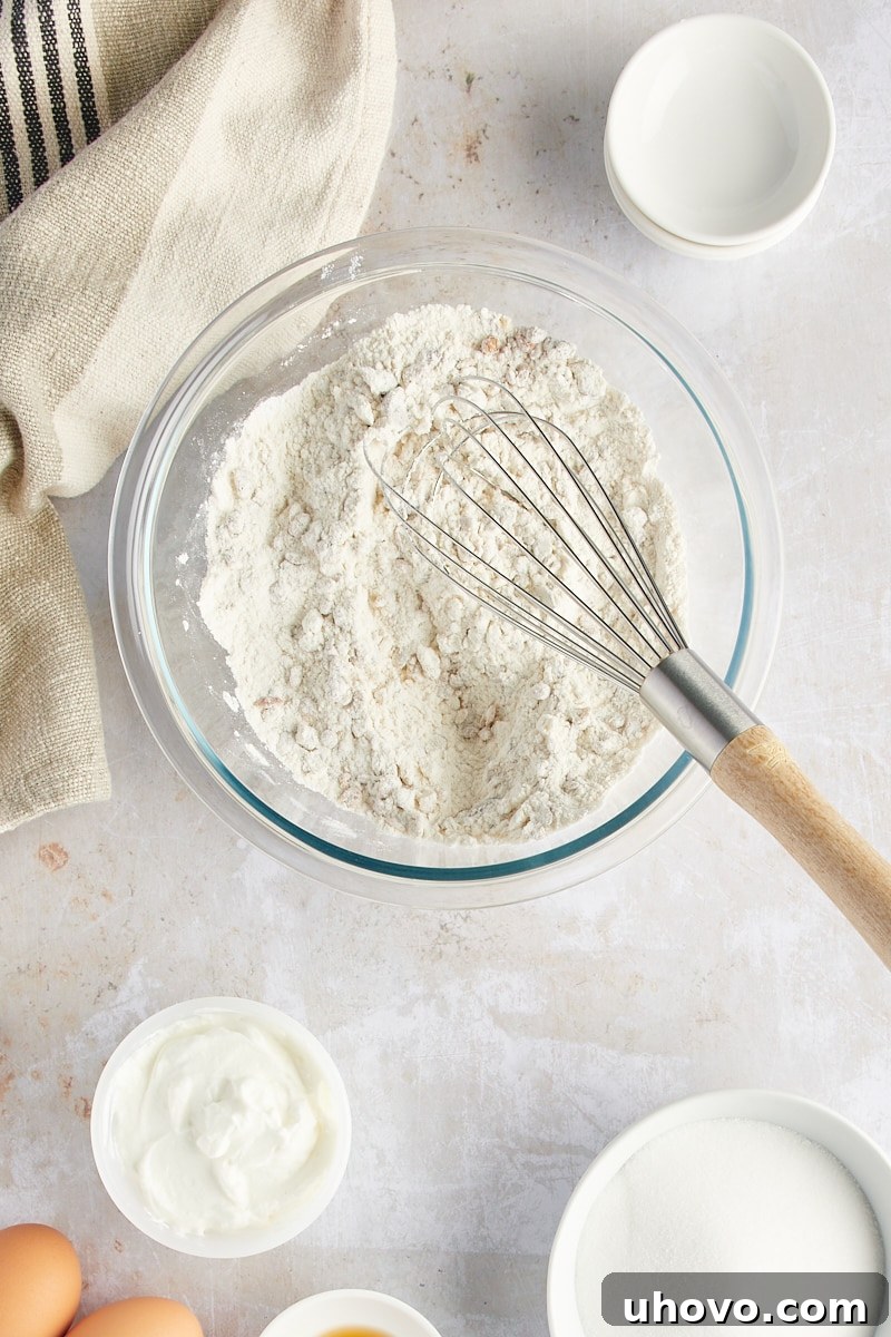 Overhead perspective of a whisk in a bowl, mixing together the dry ingredients for the granola yogurt muffins.