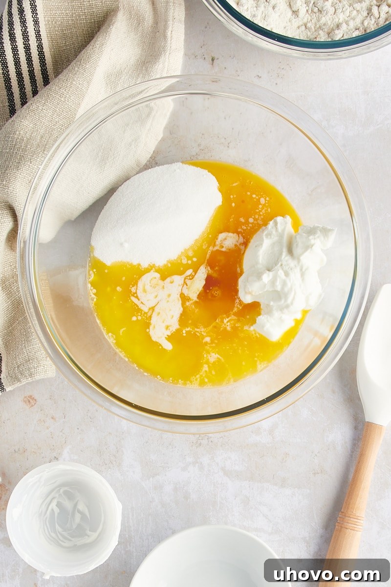 A pristine overhead view of the wet ingredients for muffins, including yogurt, melted butter, and eggs, awaiting combination.