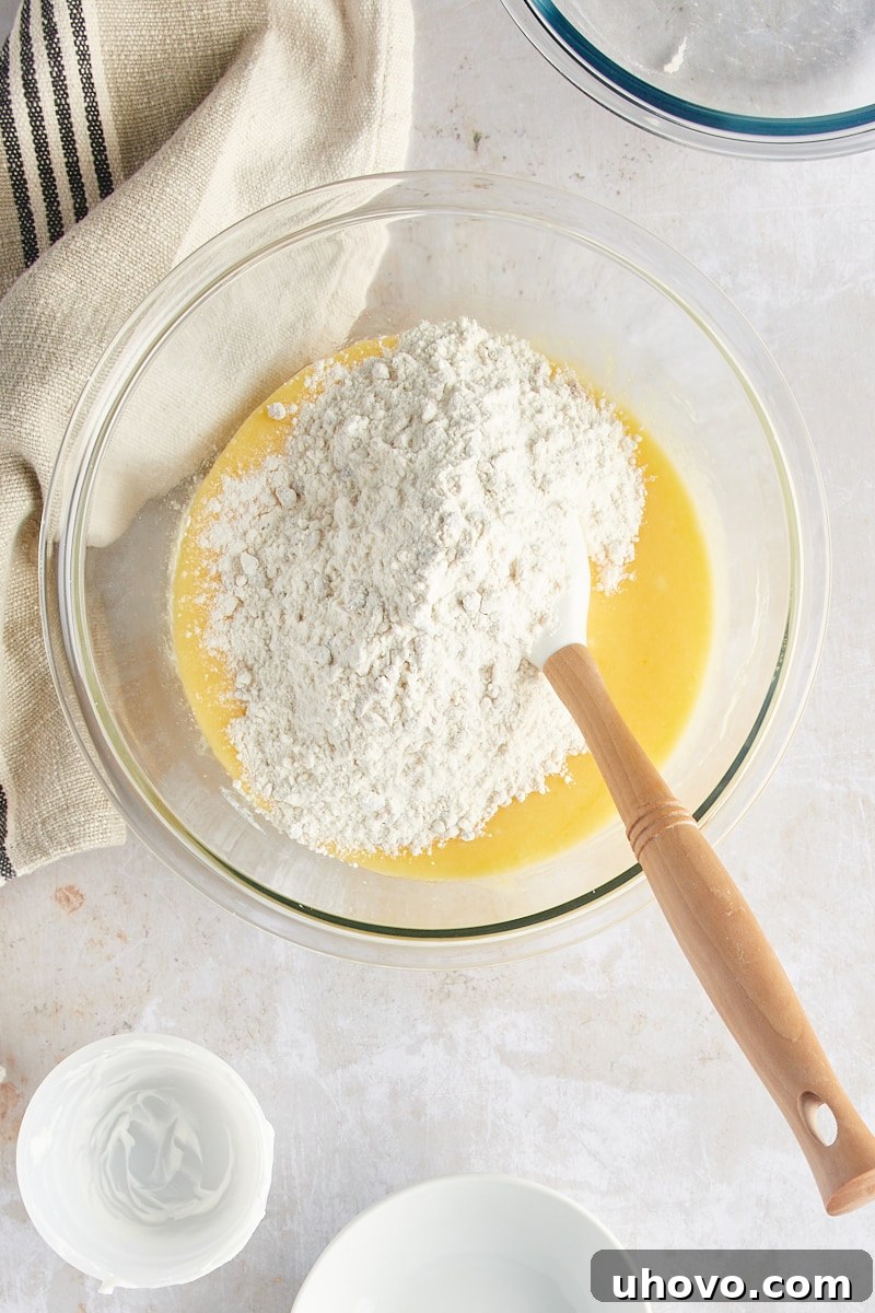A visual from above showing the dry ingredients carefully added to the wet ingredients in a glass mixing bowl, poised for gentle mixing.