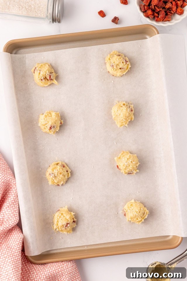 Overhead view of strawberry cream cheese cookie dough portions neatly arranged on a parchment-lined baking sheet.