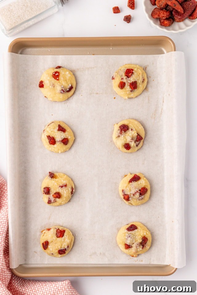 Overhead view of a batch of freshly baked strawberry cream cheese cookies with lightly golden edges on a parchment-lined baking sheet.