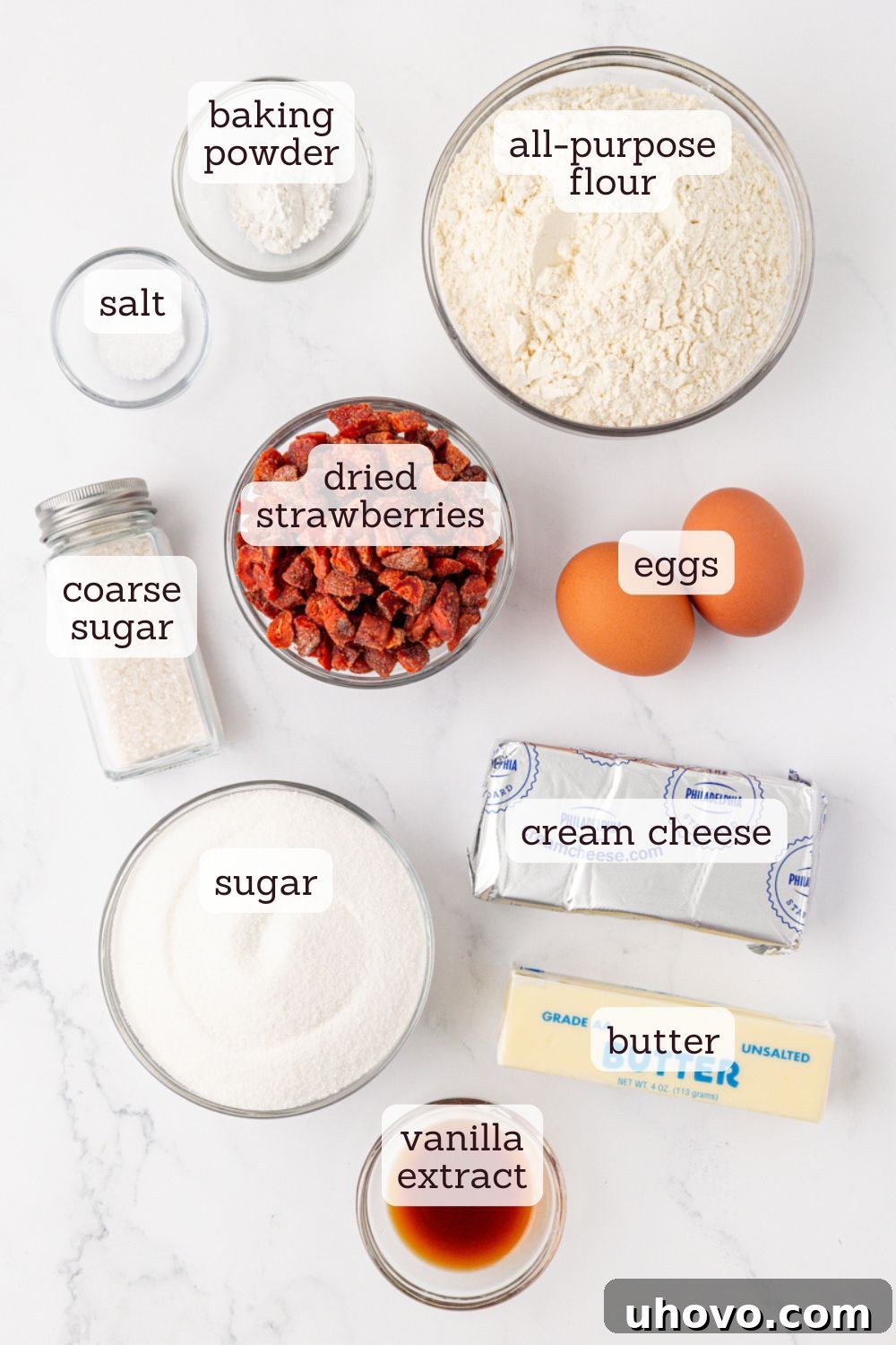 Overhead view of key ingredients for strawberry cream cheese cookies laid out, including flour, butter, cream cheese, sugar, eggs, vanilla extract, and dried strawberries.