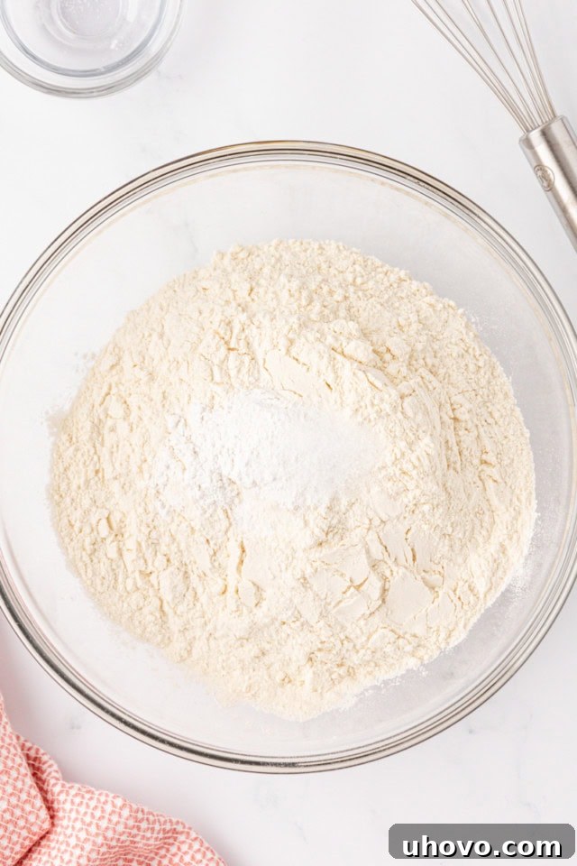 Overhead view of flour, baking powder, and salt measured into a glass mixing bowl, ready to be combined for the dry ingredients.