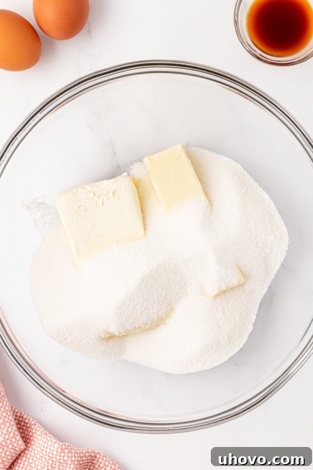 Overhead view of softened butter, cream cheese, and granulated sugar in a glass mixing bowl, about to be beaten together.