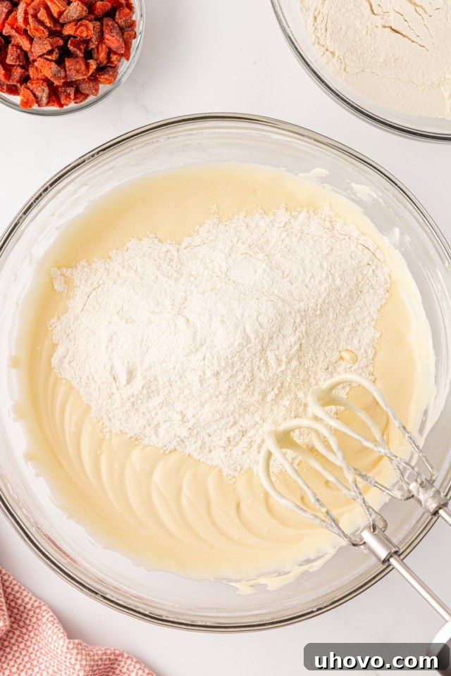 Overhead view of the dry flour mixture being gradually added to the wet cream cheese cookie dough ingredients.