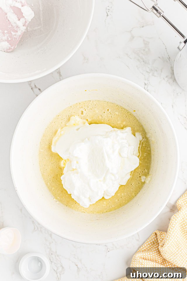The whipped egg whites being carefully added to the light lemon and sugar batter mixture.