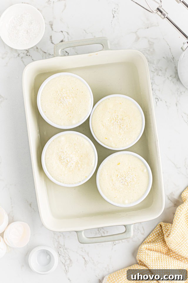 Lemon pudding cake batter divided evenly among ramekins, placed in a baking pan partially filled with hot water for a water bath.