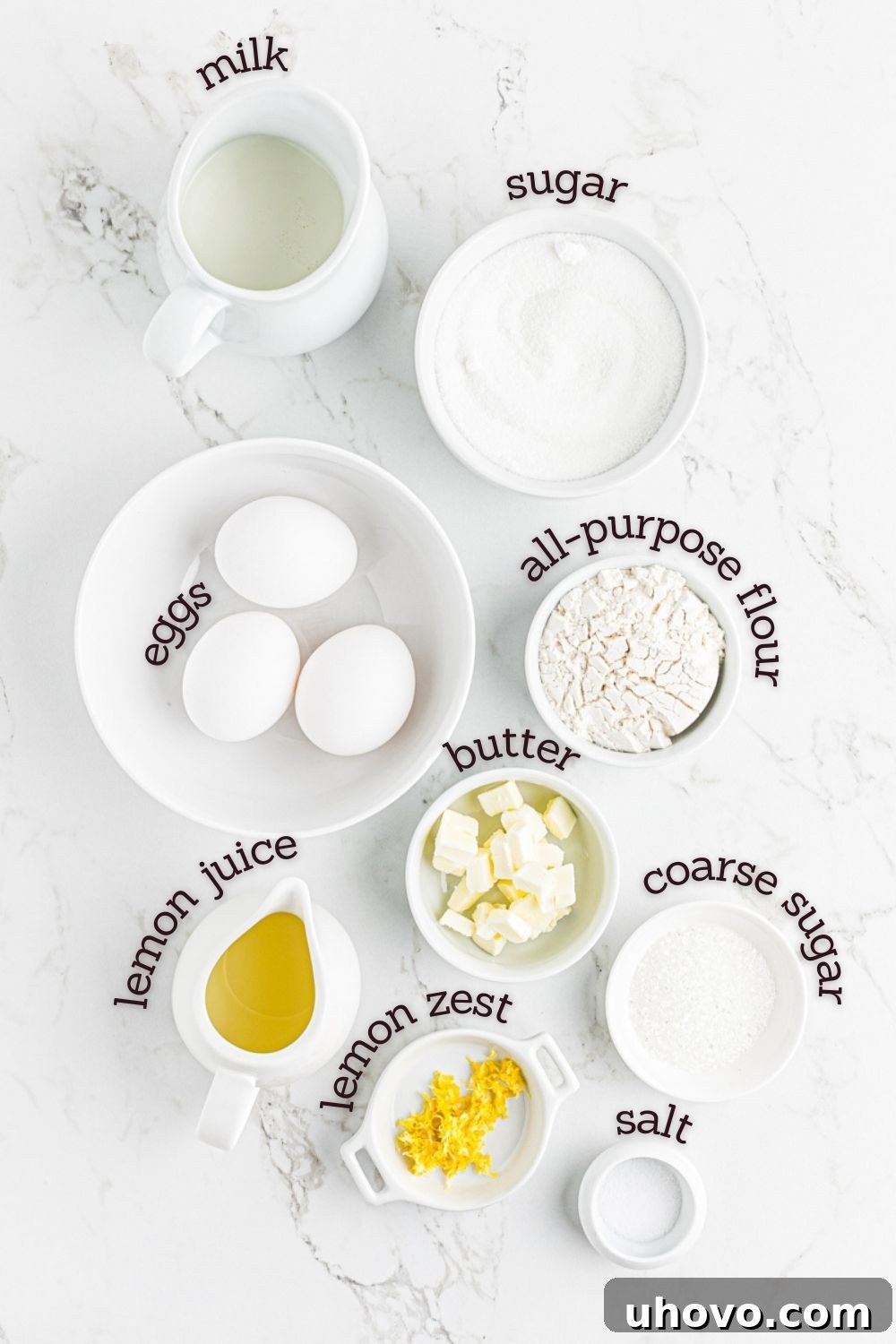 Overhead view of fresh ingredients for Meyer lemon pudding cakes laid out on a white surface.