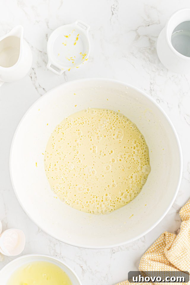 Milk, fragrant lemon zest, and fresh lemon juice being whisked into the egg yolk and butter mixture.