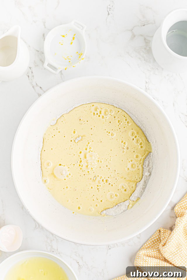 The lemon-infused liquid mixture being carefully added to the dry sugar and flour mixture.